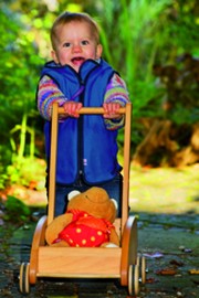 froehliches Kind beim Spaziergang mit Lauflernwagen aus Holz 